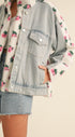 Denim jacket with floral pattern over a floral shirt on a neutral background