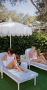 Two women sitting on lounge chairs under a large white umbrella in a garden setting.